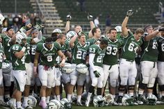 a group of football players standing on top of a field with their hands in the air