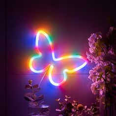 a neon butterfly is lit up on the wall next to flowers and a vase with water