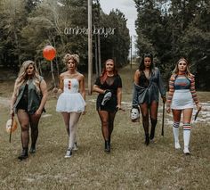 four women dressed in halloween costumes are walking through the grass with balloons and baseball bats