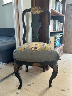 an old chair is upholstered with fabric on the seat and back, in front of a bookshelf