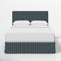 an upholstered bed with white pillows and blue pinstripe bedspread