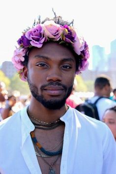 a man with flowers in his hair is wearing a white shirt and necklaces while looking at the camera