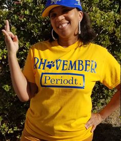 a woman in a yellow shirt and blue hat posing for the camera with her hand up