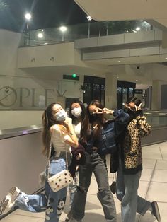 three women wearing face masks while standing in front of an airport lobby with luggage on the ground