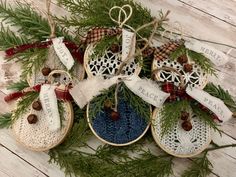 four christmas ornaments hanging from the side of a wooden table next to pine cones and evergreen branches