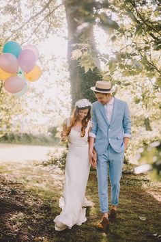 a bride and groom walking through the woods with balloons