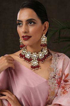 This necklace set boasts of an opulent polki design inspired by florals. This beautiful design is finished off with red stones with pearl trinkets dangling from its bottom. Necklace Closure - Adjustable Dori Earrings Closure - Push Back Style Tip - Ace the festive season in this statement necklace set worn with anything traditional starting from pastel lehengas to solid hued sarees. This pretty is perfect for the woman in love with the little details of her rich traditional heritage that is remi Elegant Red Kundan Necklace, Festive Red Ruby Jewelry Set, Red Kundan Set With Stone Work, Red Chandbali Temple Necklace With Stone Work, Red Stone Work Sets For Gifts, Red Sets With Stone Work For Gift, Red Jeweled Bollywood Jewelry, Red Kundan Sets For Gift, Red Meenakari Chandbali Necklaces