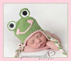 a baby wearing a crocheted frog hat and sleeping on top of it's head