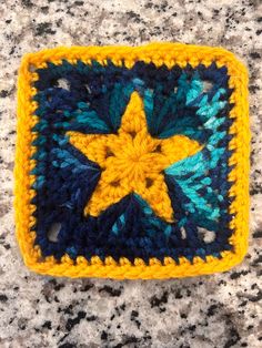 a crocheted square with a yellow and blue star in the center on a granite surface