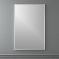 a square mirror mounted to the side of a wall next to a shelf with a vase on it