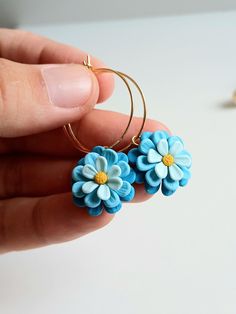 a person holding two small blue flowers in their hand and one is wearing a gold hoop earring