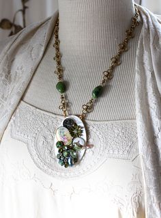 "Soft olive and creamy pearl colors create a reminiscent pendant necklace, so feminine, elegant and delicate. An antique mother of pearl buckle, long and oval, with sift pearly white tones in the light, forms the base for this piece. I've selected 3 vintage pieces, 3 antique buttons (the hand painted porcelain floral, (mid left), and the two buttons above and below) to adorn the buckle. There is also a bezel sealed with a glass dome. It contains a clipping from an antique postcard of a quaint co Victorian Oval Green Necklace, Green Vintage Charm Jewelry For Weddings, Green Vintage Charm Jewelry For Wedding, Green Vintage Charm Wedding Jewelry, Elegant Green Jewelry With Vintage Charm, Vintage Long Pearl Pendant Necklace, Vintage Pearl Pendant Jewelry, Handmade Victorian Green Necklaces, Vintage Oval Pearl Pendant Jewelry