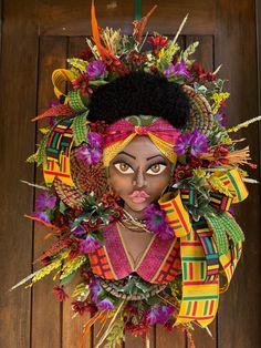 an african woman's head is adorned with colorful flowers and leaves in front of a wooden door