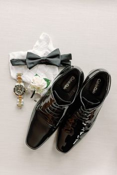 a pair of black shoes sitting next to a watch and white boutonniere