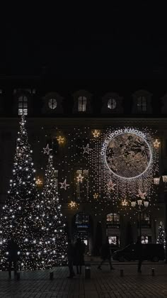 a large christmas tree is lit up in front of a building with lights on it