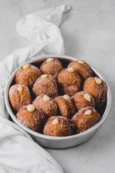 a bowl filled with powdered sugar covered donuts on top of a white cloth