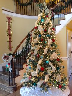 a decorated christmas tree sitting in the middle of a living room next to a staircase