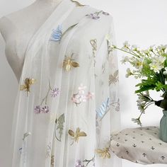 a white scarf with flowers and butterflies on it next to a vase full of flowers