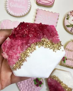 a hand holding a piece of pink and gold glittered sugar with cookies in the background