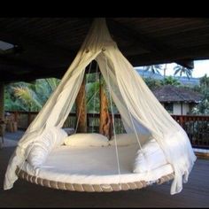 a white bed hanging from the ceiling in a room with wooden floors and palm trees