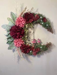 a wreath with red flowers and greenery hanging on the wall next to a mushroom