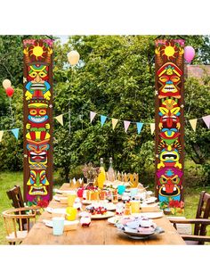 a wooden table topped with plates and cups filled with food next to tall poles covered in decorations