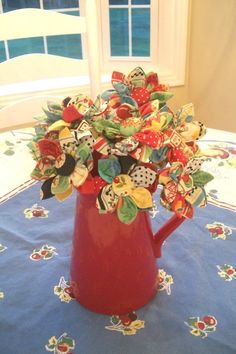 a red pitcher filled with lots of colorful buttons on top of a blue table cloth