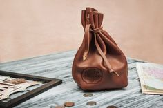 a brown leather bag sitting on top of a wooden table next to some coins and money