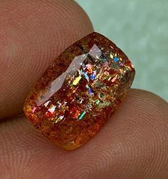 a close up of a person's hand holding a piece of orange colored diamond