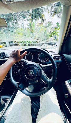 a person driving a car with their hands on the steering wheel and dashboard, in front of palm trees