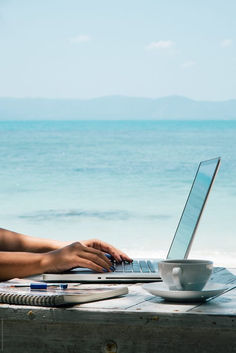 a woman sitting at a table with a laptop computer on her lap by the ocean