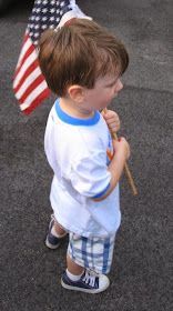 a little boy holding an american flag and standing in the street