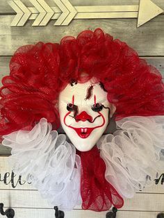 a creepy clown mask with red hair and white face is hanging on a wooden wall