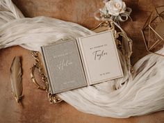 an open book sitting on top of a table next to some feathers and a flower