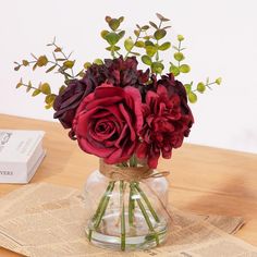 a vase filled with red flowers sitting on top of a table next to a book