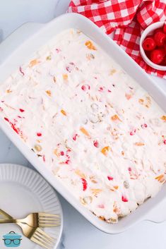 a white dish filled with fruit and topped with icing next to a bowl of cherries