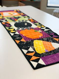 a colorful table runner on top of a white table with black and orange designs in the center