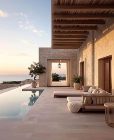 an outdoor living area with couches and tables next to a swimming pool at sunset