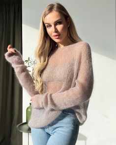 a woman is posing for the camera in jeans and a pink sweater with long sleeves