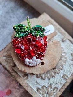 an apple shaped brooch sitting on top of a piece of wood