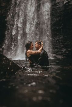 a man and woman are kissing in front of a waterfall with water cascading over them