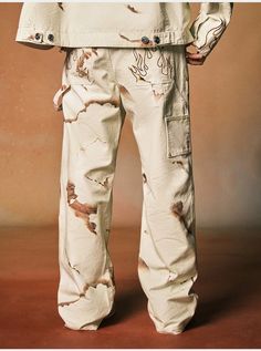 a man wearing white pants with paint splattered all over it and his hands in his pockets