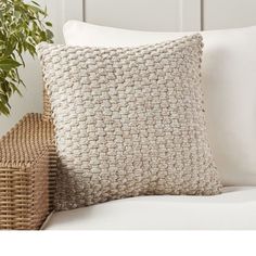 a close up of a pillow on a couch next to a basket with a plant