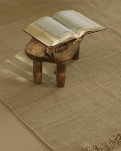 an open book sitting on top of a wooden bench next to a rug with tassels