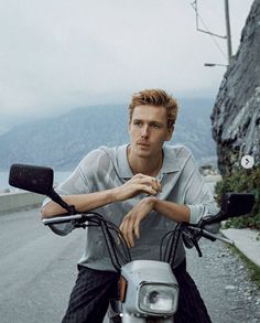 a man sitting on the back of a scooter next to a mountain road