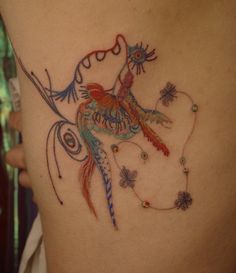 a colorful bird tattoo on the side of a woman's stomach, with butterflies and beads