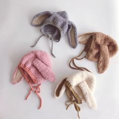 four knitted hats are lined up on a white surface, one is pink, the other is brown