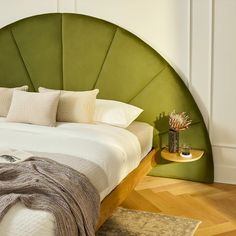 a bedroom with a green headboard and white bedding on top of wooden flooring