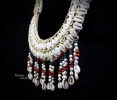 Papua New Guinea traditional tribal cream braided rope necklace, decorated with white Cowrie Shells, small cream Nassa Shells, and a fringe of black painted wooden beads, red and white seeds, each ends with a white Cowrie Shell. The upper band of the collar are round wooden beads and circular white shells. The inner diameter of the necklace is 5 inches, and the outer diameter is 10.25 inches. The seed fringe is 3 inches in drop length, and the overall drop length of the necklace is 16 inches. So White Macrame Necklace For Festivals, White Macrame Necklace For Festival, White Braided Jewelry For The Beach, White Braided Jewelry For Beach, White Braided Jewelry Gift, White Braided Jewelry As A Gift, Handmade White Bohemian Necklaces, Bohemian White Necklaces For Festival, Bohemian White Necklace For Festival