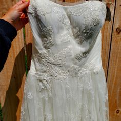 a white dress is being held up against a wooden fence by someone's hand